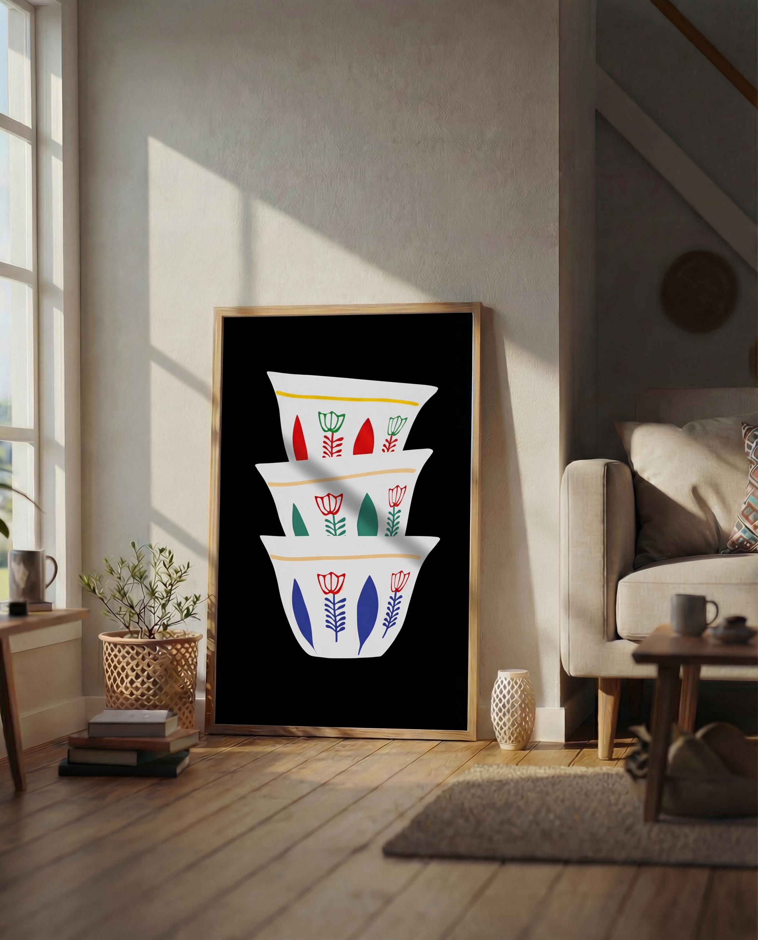 A framed art print featuring a stack of three white coffee cups with colorful floral designs. The cups have red, green, and blue accents. The artwork is set against a black background.