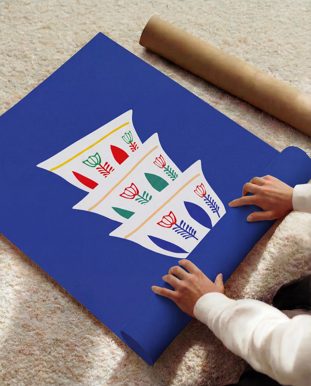 A rolled blue poster with a white graphic of stylized coffee cups with red, green, and yellow floral designs. A brown paper tube is visible in the background. The poster is being unrolled.