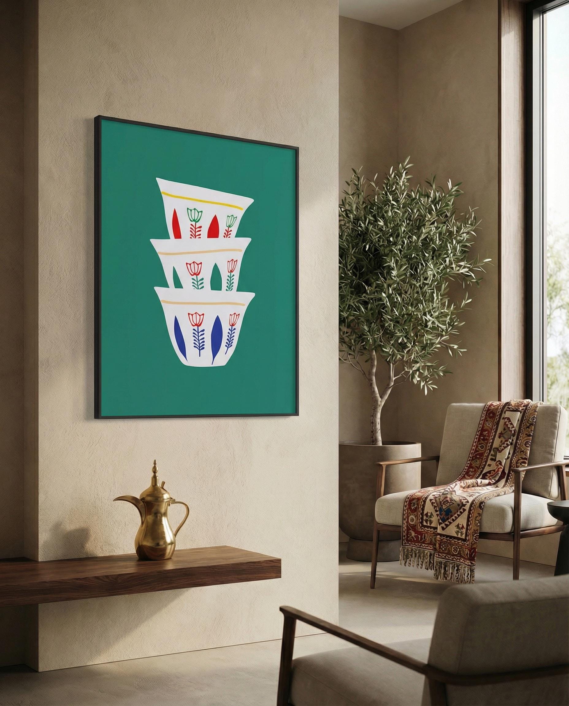 A framed art print featuring a stack of three white coffee cups with red, blue, and yellow floral designs against a teal background. The artwork is displayed in a modern living room setting.